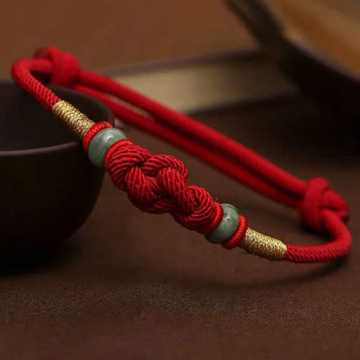 Red braided unity knot bracelet with two green jade rings and gold-colored thread accents.